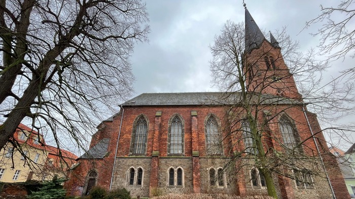 Alte Kirche aus Backstein mit hohem Turm und leerer Bank davor