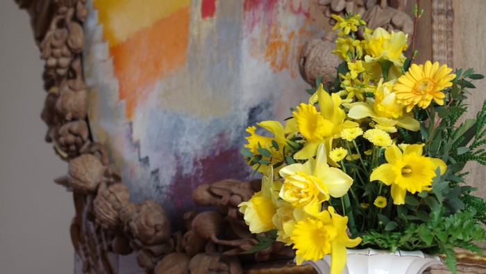 En blomsterstang med gule blomster på en bord med bøger og en maleri