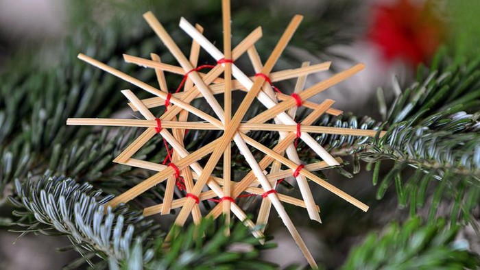 Ein selbstgebastelter Weihnachtsstern aus Holzstöcken hängt an einem Tannenbaum.