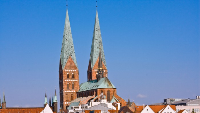 Zwei hohe Kirchtürme vor blauem Himmel in kleiner Stadt.