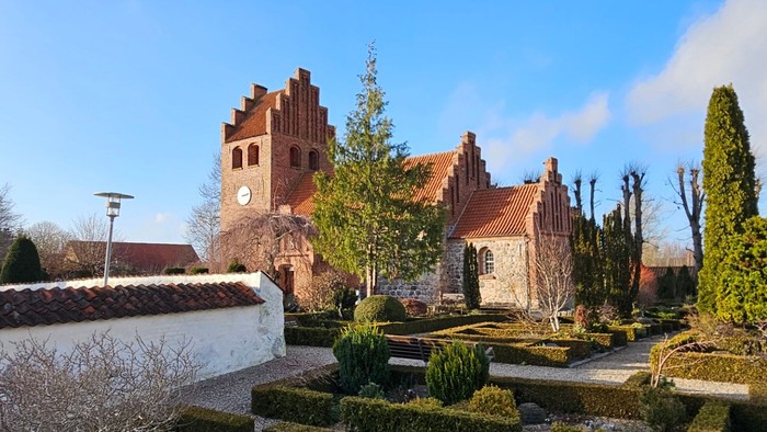 En smuk have med formede hegn og en stor kirke i baggrunden