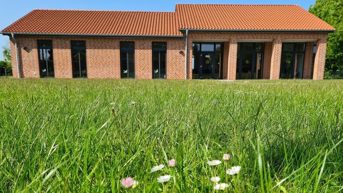 Ein rotes Backsteingebäude mit hohem Gras und Blumen im Vordergrund