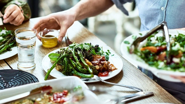 En gruppe af mennesker deler en mad, der består af salater og pizza, på en træbord.