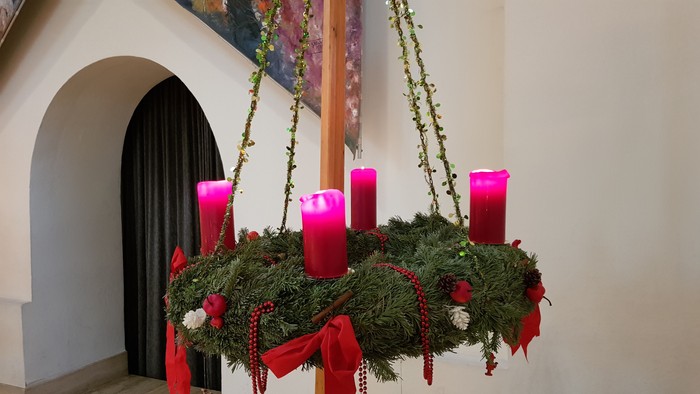 Ein Adventskranz mit vier pinken Kerzen hängt an einem Holzpfosten