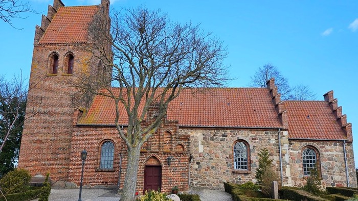 En gammel kirke med teglmur og røde tag.