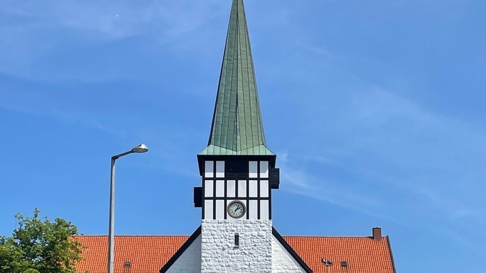 En hvid kirke med spiret og klokke, omgivet af andre huse med røde tag.