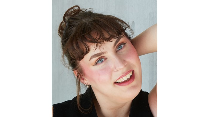 En ung kvinde med kort hår og blå øjne smiler til kameraet.