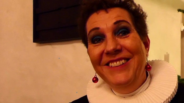 En kvinde med hvid krage og røde øreringe smiler til kameraet.