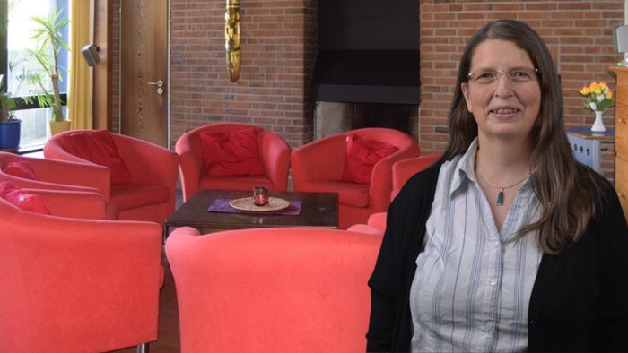 Frau sitzt in rotem Sessel in gemütlichem Raum