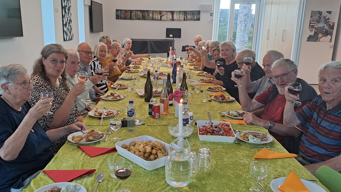 En gruppe af personer sidder til middag på en lang bord med mad og drikkevarer