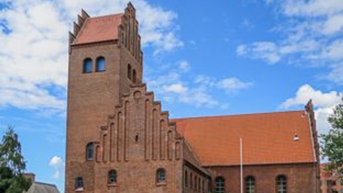 En rød murstenskirke med tårn og spidskærme, beliggende ved en gade med cykler.