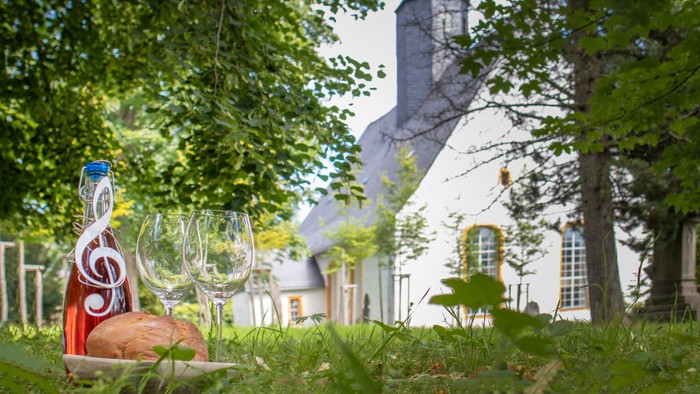 Weinflasche und Gläser vor Kirche im Grünen
