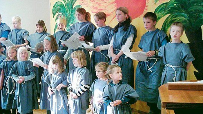Kinder in blauen Gewändern, die in einem Chor singen.