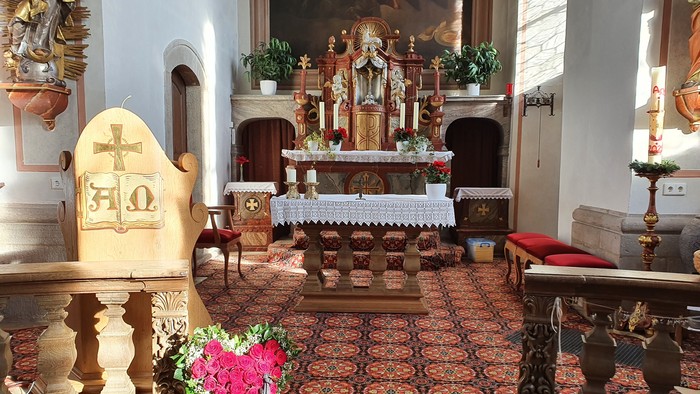 Innenraum einer Kirche mit Altar, Kreuz und Blumen.