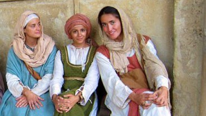 Drei Frauen in traditioneller Kleidung posieren vor einer Steinmauer