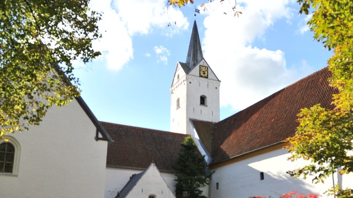 En hvid kirke med tårn og træer med faldne blade.