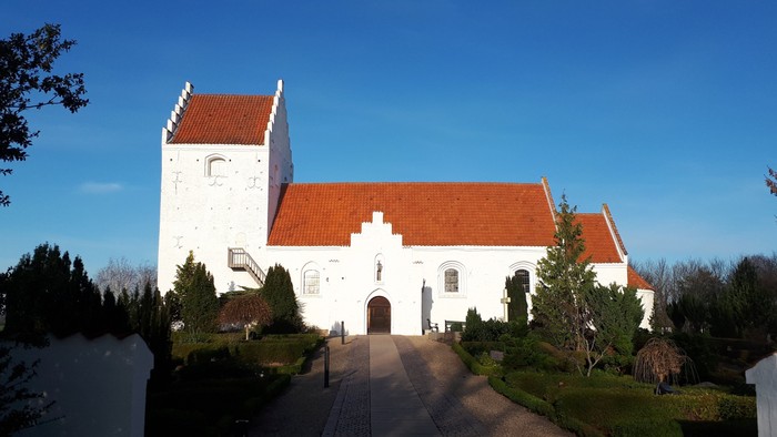 Et hvidt kirkebygning med røde tag og en smuk have foran