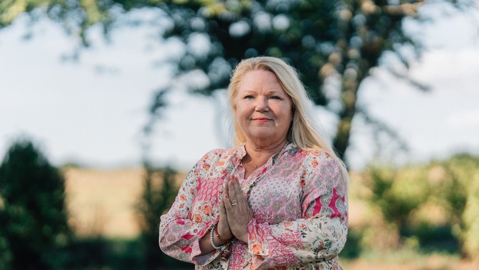 En kvinde står i en park og har hænderne samlet foran sig.