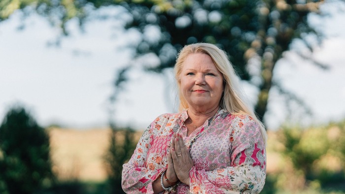 En kvinde står i en park og har hænderne samlet foran sig.