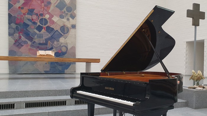 Ein schwarzes Klavier steht in einem Raum mit einem Kreuz und einem abstrakten Gemälde.