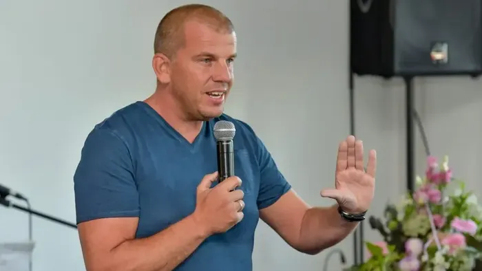 Ein Mann in blauem Hemd spricht in ein Mikrofon und gestikuliert.