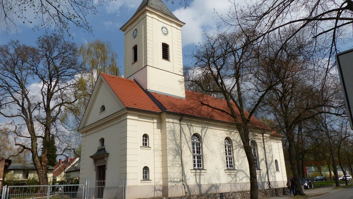 Kleine weiße Kirche mit rotem Dach und Turm in parkähnlicher Umgebung