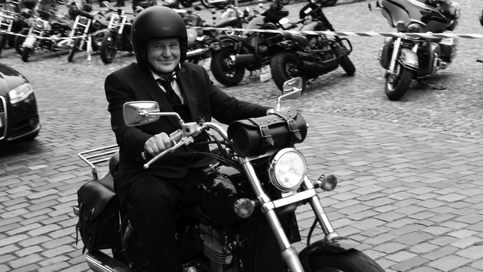 Mann in Anzug fährt Motorrad durch Kopfsteinpflasterstraße