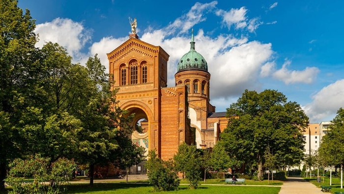 Großer Backsteinkirchturm mit grüner Kuppel in Parklandschaft