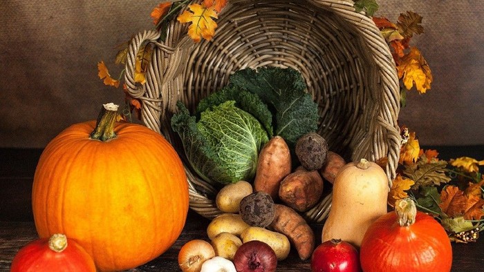 Ein Korb gefüllt mit Herbstgemüse und Kürbissen auf einem Holztisch