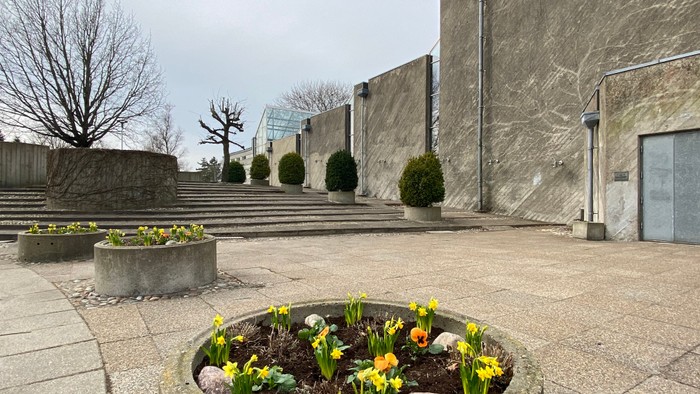 En træppeopstilling med blomster og buske foran et stort murværk