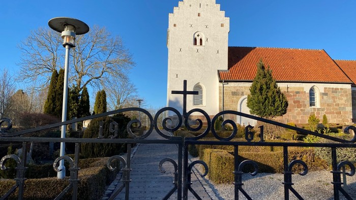 En smuk kirke med tårn og murværk, omgivet af en stykket mur og en lampost.