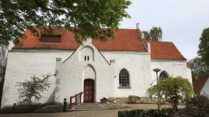 Et smukt hvidt kirkebygning med røde tag og fine blomsterbænke foran