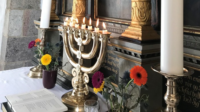 En altertavle med lysstake og blomster i kirke