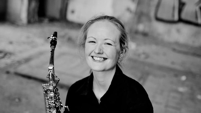 En kvinde med blågul hår holder en saksofon og smiler.