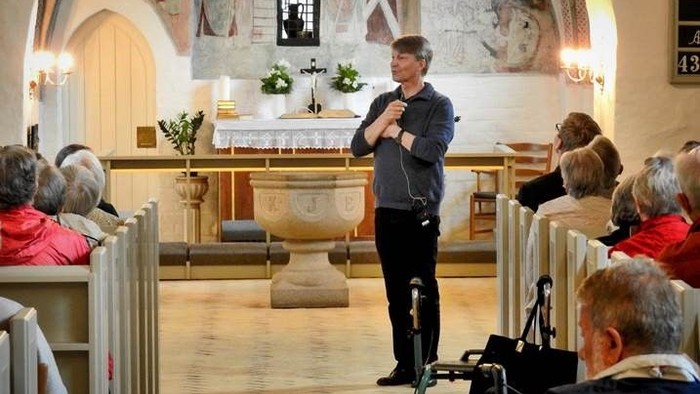 En mand står og tale i en kirke, mens en kamera holdes op på en tripod.