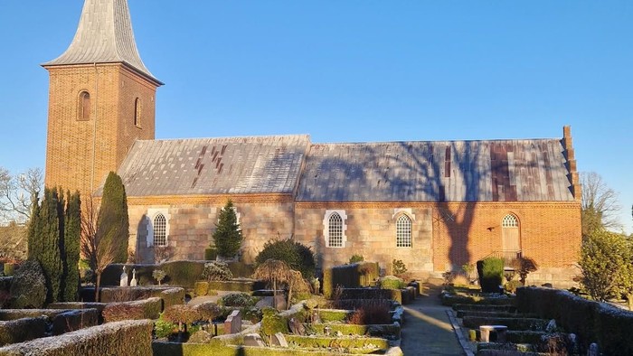 En kirke med tårn og en have med buske og stier