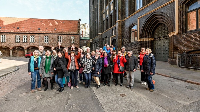 Eine Gruppe von Menschen posiert vor einem historischen Gebäude mit Ziegelmauerwerk und großen Bögen.