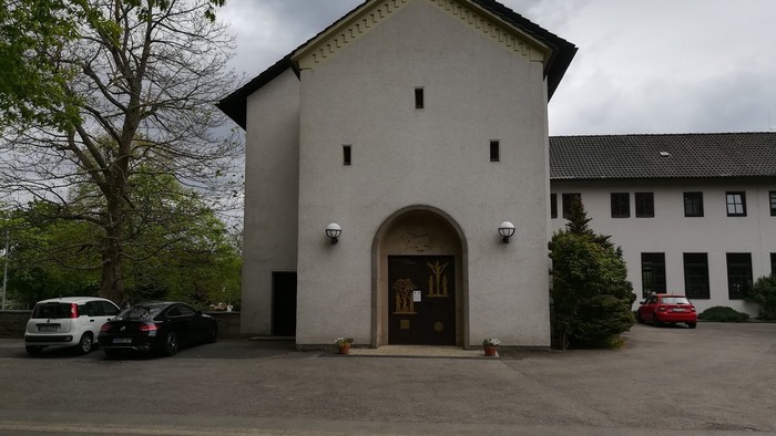 Das Bild zeigt ein weißes Gebäude mit einem Torbogen und mehreren geparkten Autos davor.