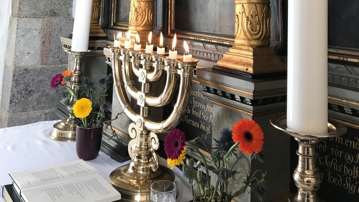 En altertavle med lysstake og blomster i kirke