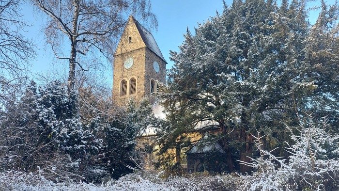 Schneebedeckte Bäume und ein Kirchturm mit Uhr im Winter