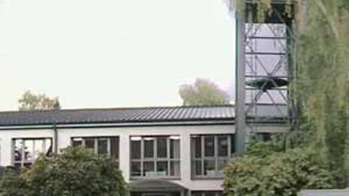 Das Bild zeigt ein modernes Gebäude mit einem hohen Turm und umgeben von Bäumen.