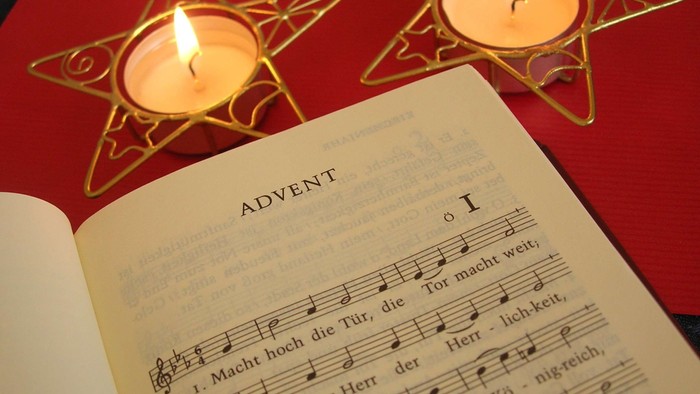 Kerzen in Sternhaltern neben einem geöffneten Adventsliederbuch