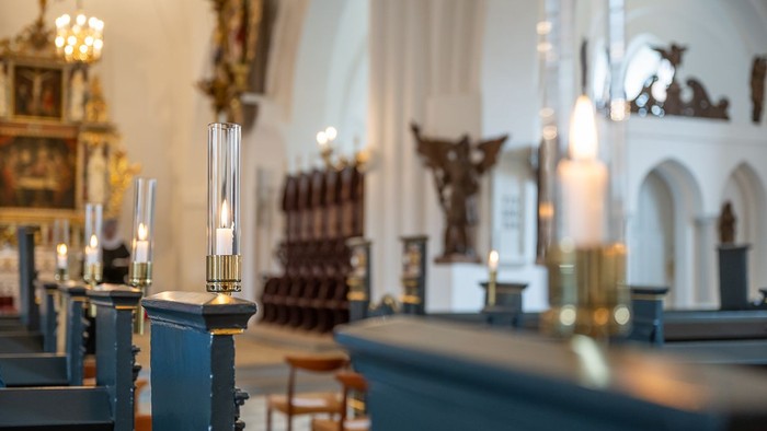 Indre del af en kirke med blå bænke og lysende kandle.