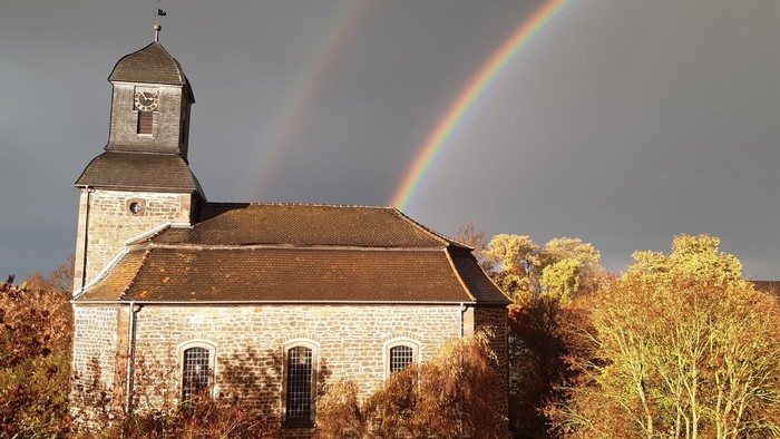 Kirche mit doppeltem Regenbogen und Herbstbäumen.