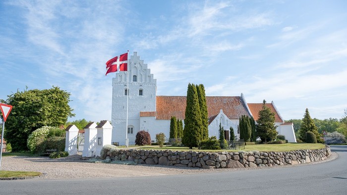 En hvid kærmisk tårn med rødt tag og dansk flag på en stenmur ved en vej
