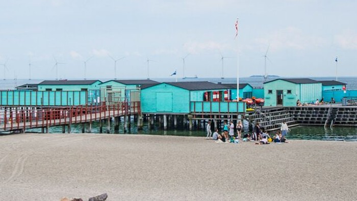 Blå strandhuse på stokværker ved stranden med mennesker og børn.