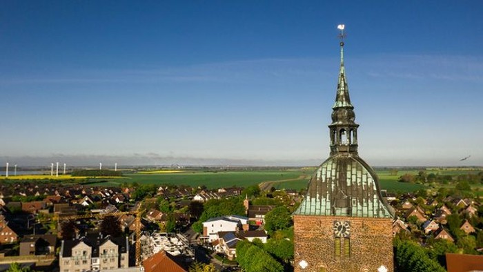 Ein Dorf mit einer Kirche und Windrädern in der Ferne unter klarem Himmel