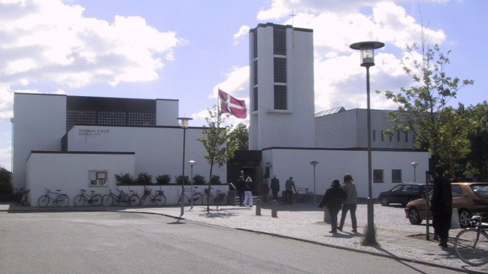 En moderne bygning med flag, cykler og mennesker i forgrunden