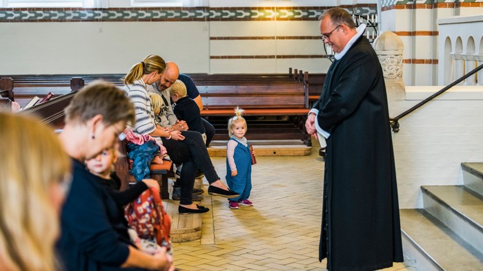 En præst taler til en gruppe børn og voksne i en kirke.