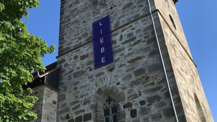Steinerner Turm mit blauem Schild und Bank.
